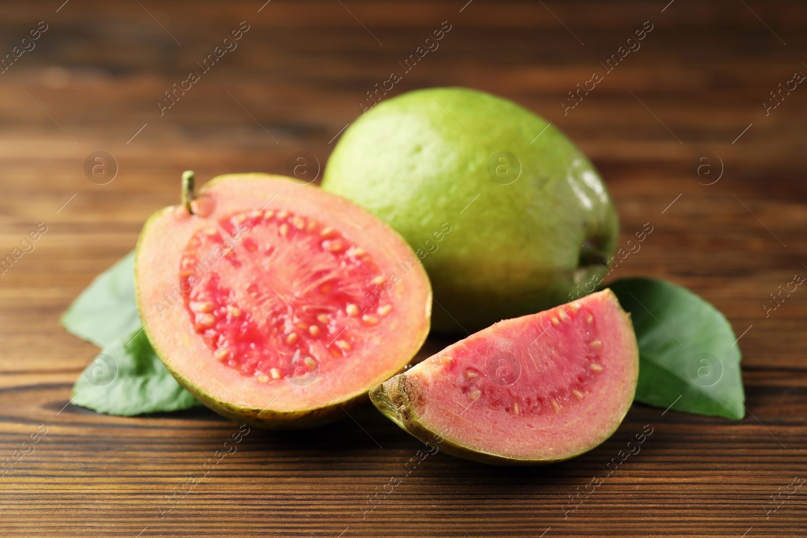 Photo of Fresh cut and whole guava fruits with leaves on wooden table, closeup