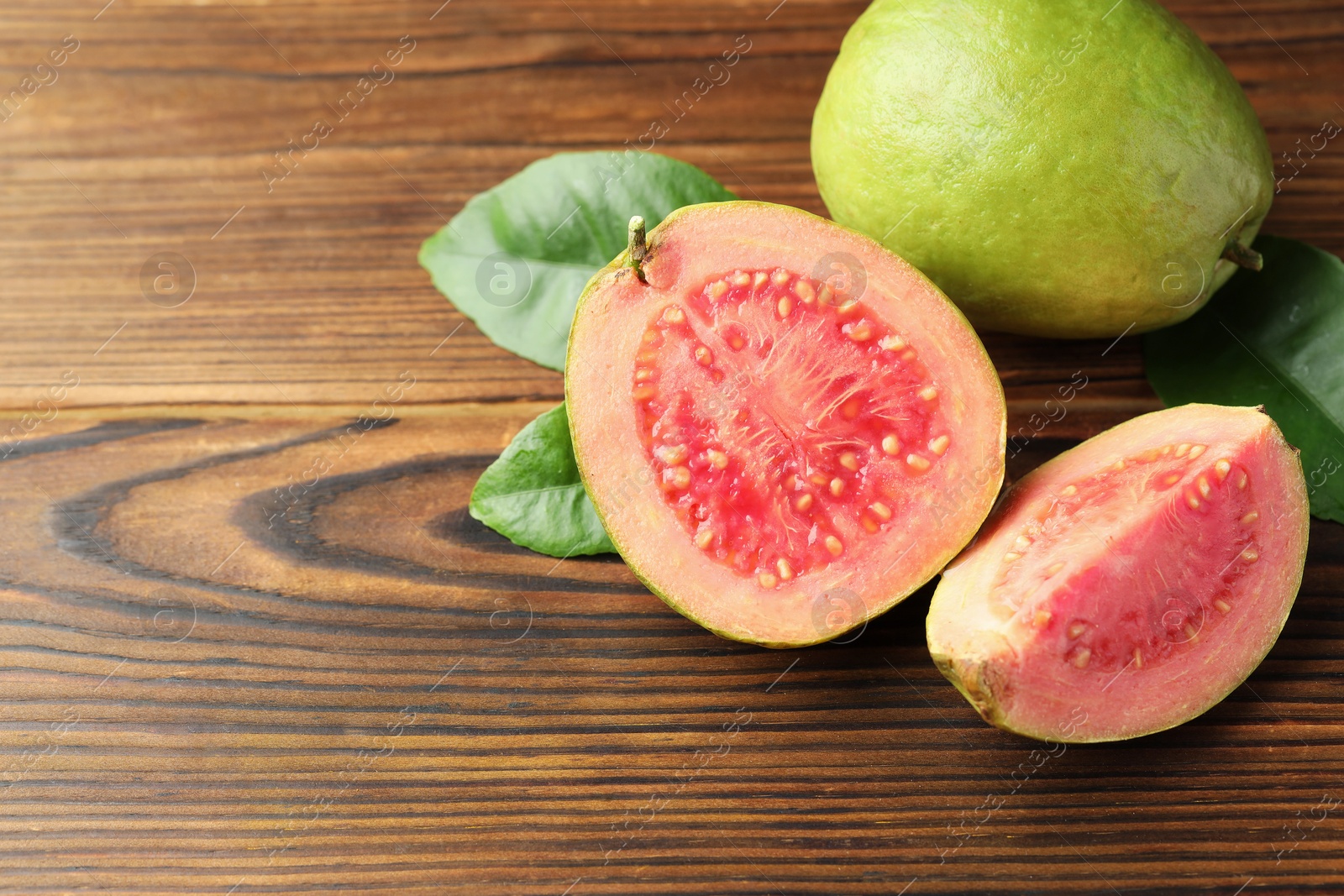 Photo of Fresh cut and whole guava fruits with leaves on wooden table, above view. Space for text