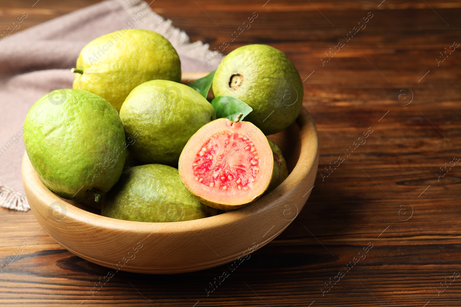 Photo of Fresh cut and whole guava fruits in bowl on wooden table, closeup