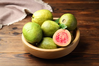 Photo of Fresh cut and whole guava fruits in bowl on wooden table, closeup