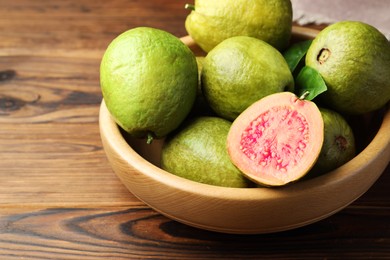 Photo of Fresh cut and whole guava fruits in bowl on wooden table, closeup