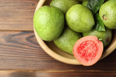 Fresh cut and whole guava fruits in bowl on wooden table, top view. Space for text