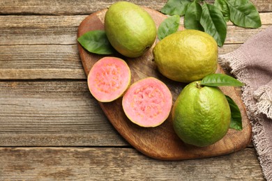 Photo of Fresh whole and cut guava fruits on wooden table, flat lay. Space for text