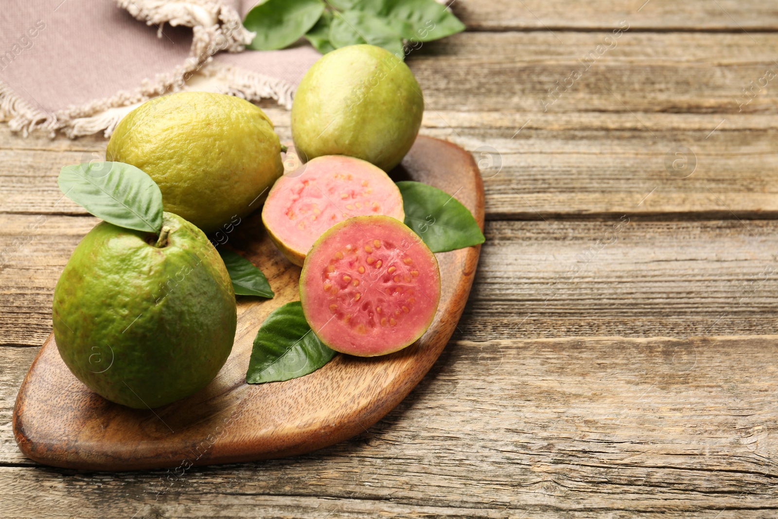 Photo of Fresh whole and cut guava fruits on wooden table, closeup. Space for text