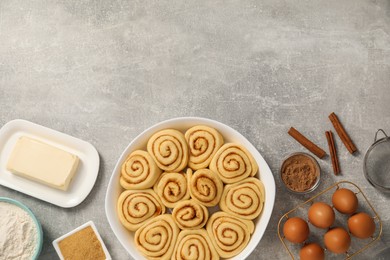 Photo of Raw cinnamon rolls in baking dish and different ingredients on grey table, flat lay. Space for text