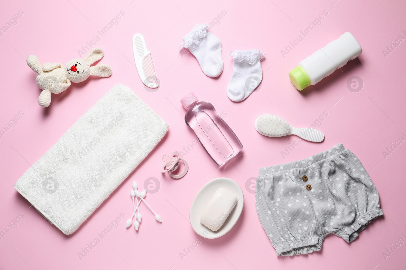 Photo of Baby oil, clothes and bath accessories on light pink background, flat lay