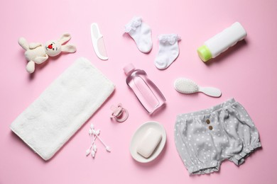 Photo of Baby oil, clothes and bath accessories on light pink background, flat lay