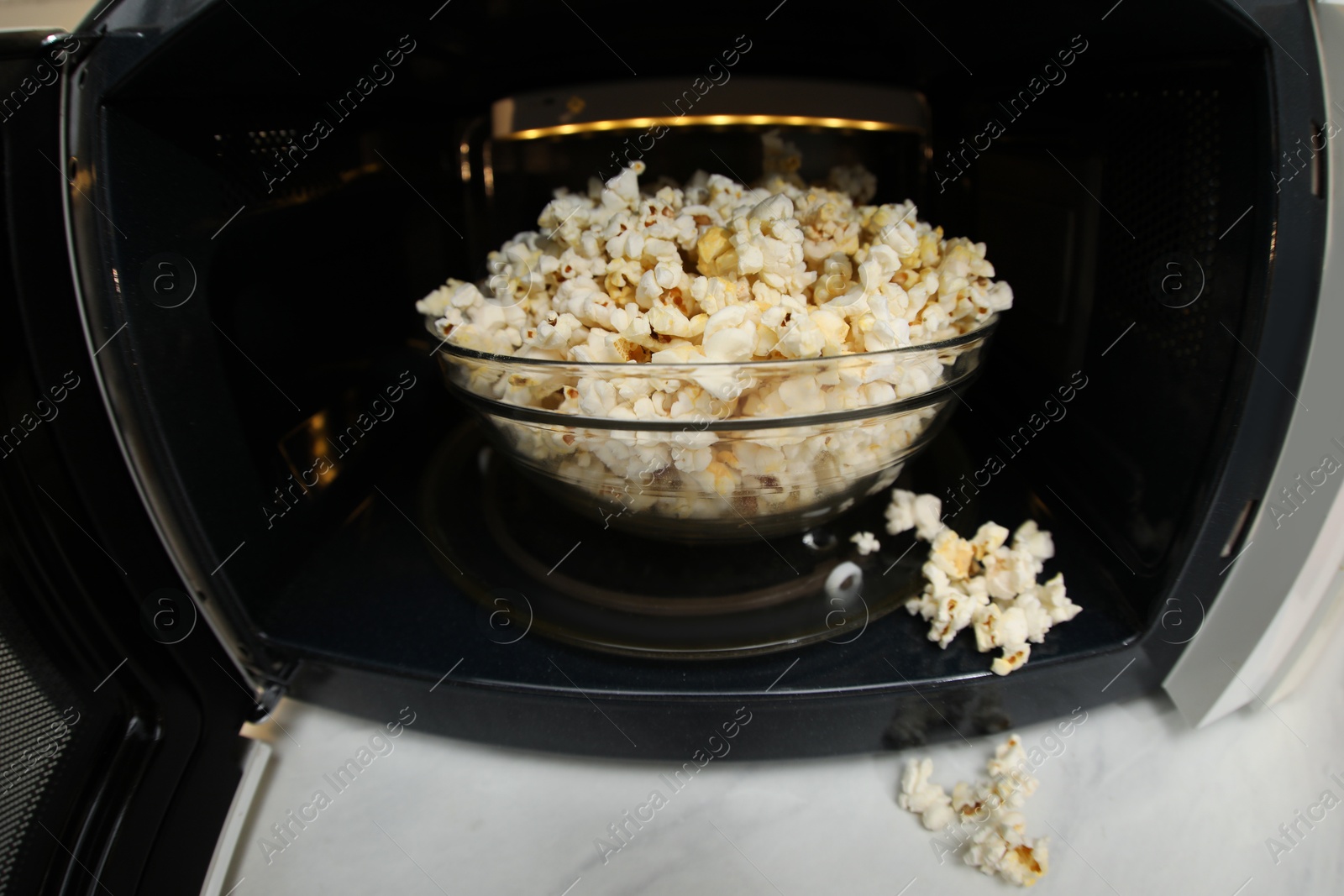 Photo of Bowl of tasty popcorn in microwave oven on white marble table, closeup. Fisheye lens effect