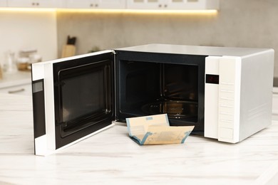 Photo of Open microwave oven and bag of popcorn on white marble table in kitchen