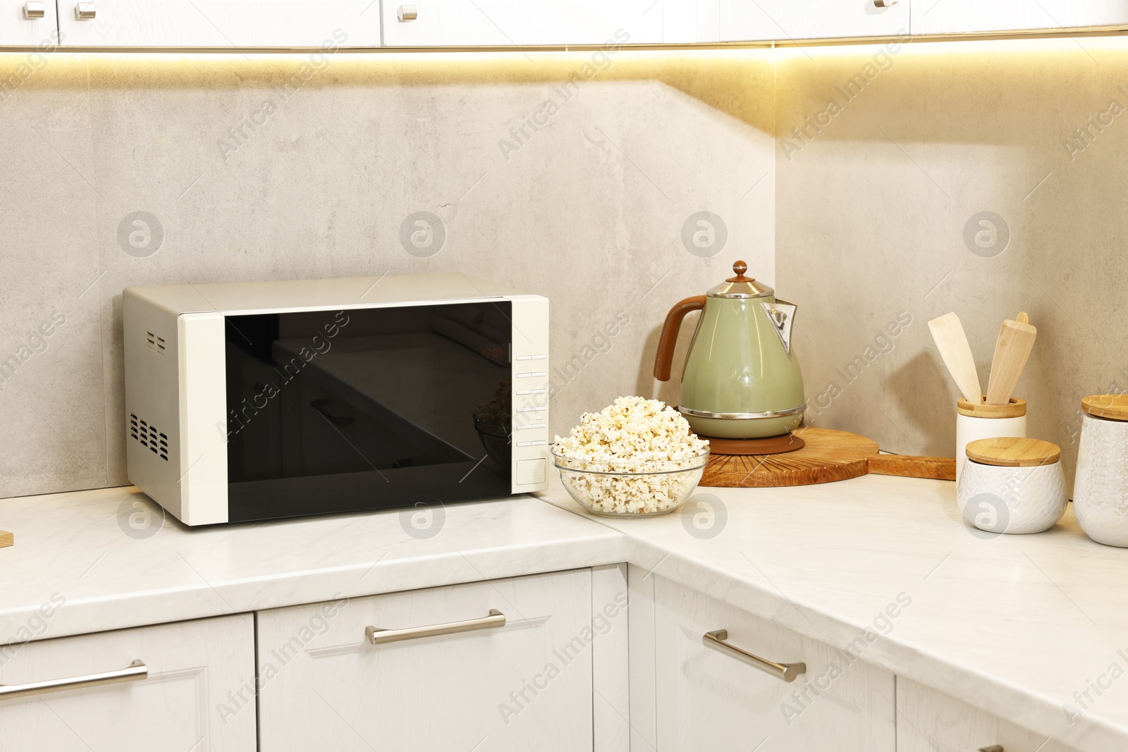 Photo of Tasty popcorn in bowl near microwave oven on white marble countertop indoors