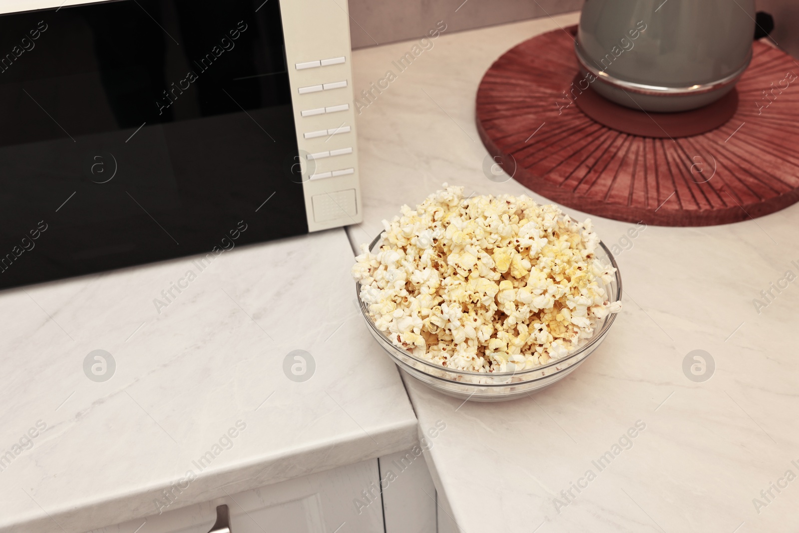 Photo of Tasty popcorn in bowl near microwave oven on white marble countertop indoors