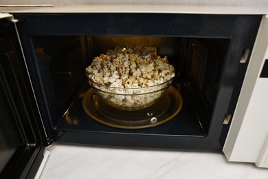 Photo of Bowl of tasty popcorn in microwave oven, closeup