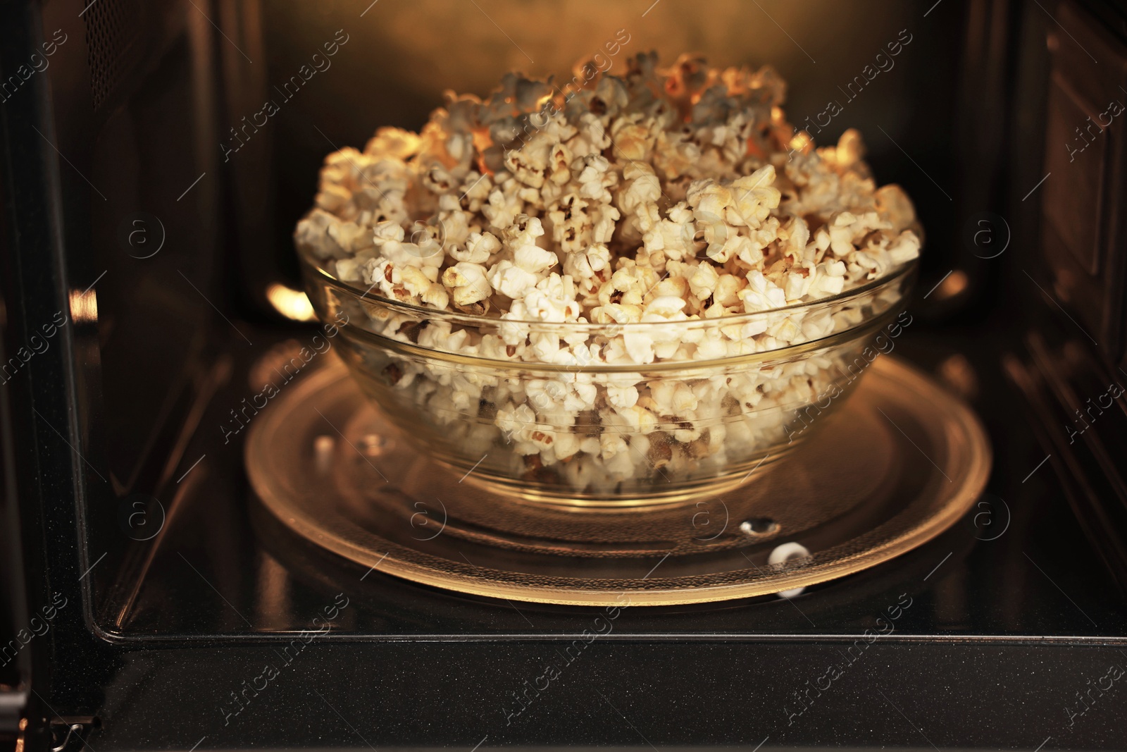 Photo of Bowl of tasty popcorn in microwave oven, closeup