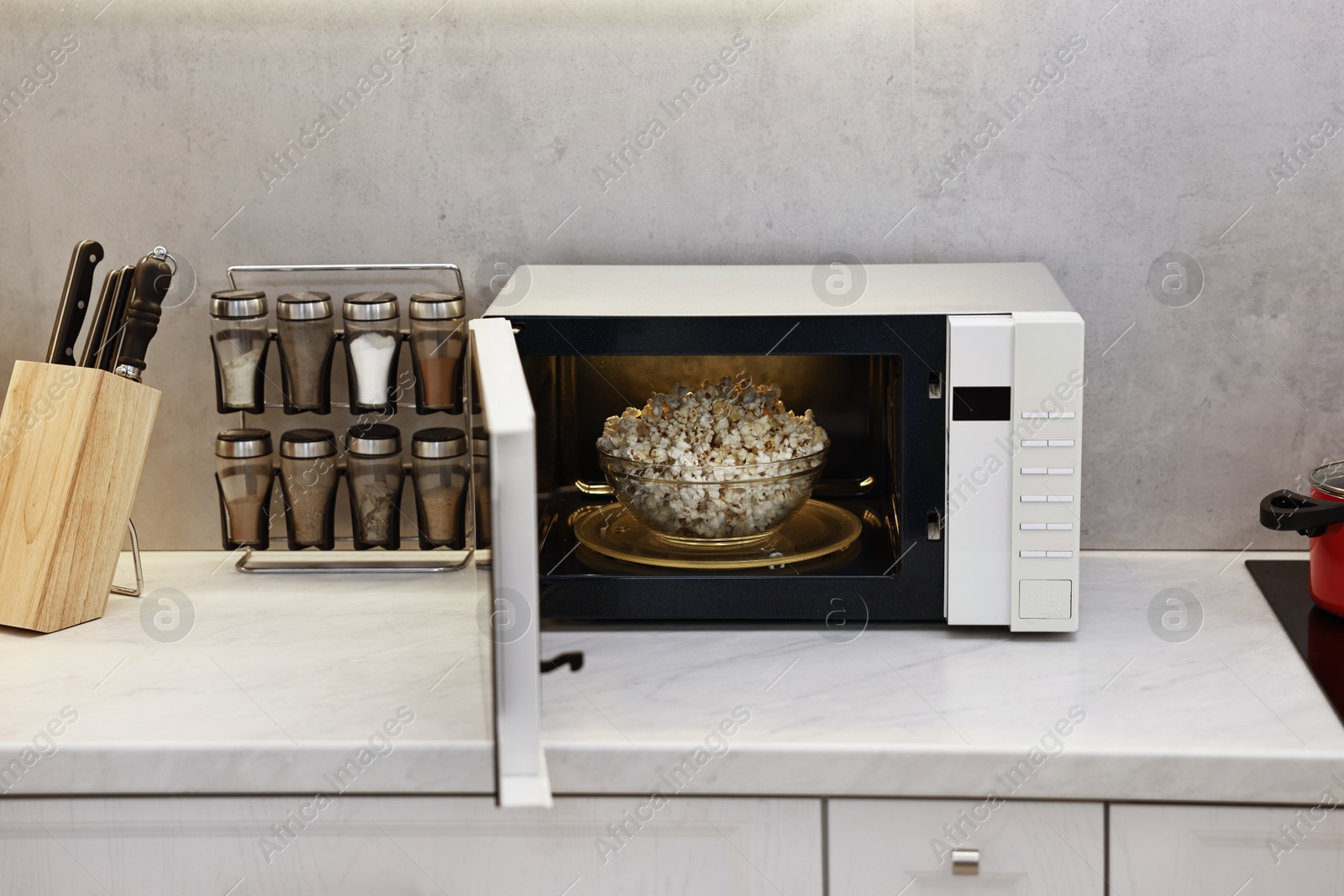 Photo of Open microwave oven with bowl of popcorn on white marble countertop in kitchen