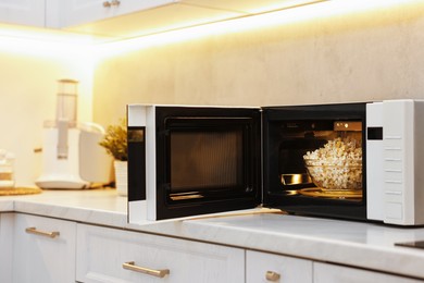 Photo of Open microwave oven with bowl of popcorn on white countertop in kitchen