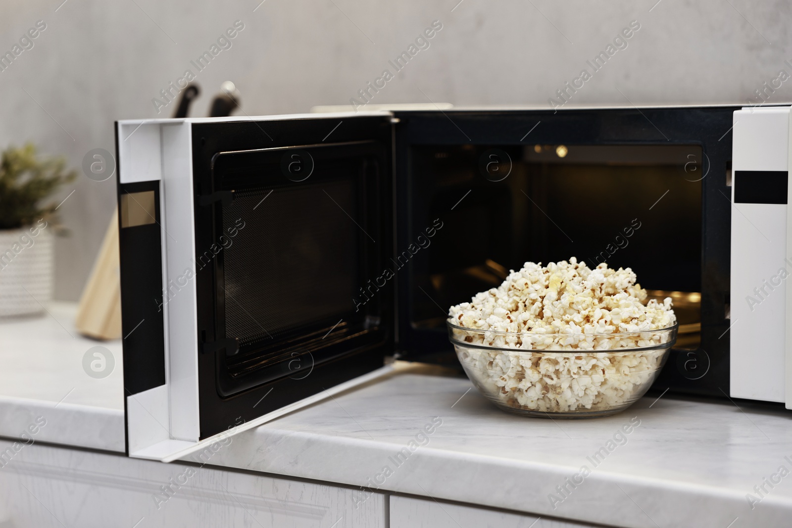 Photo of Tasty popcorn in bowl near microwave oven on white marble countertop indoors