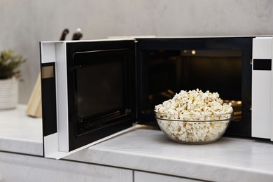 Photo of Tasty popcorn in bowl near microwave oven on white marble countertop indoors