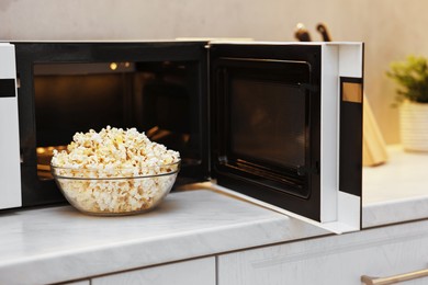 Photo of Tasty popcorn in bowl near microwave oven on white marble countertop indoors