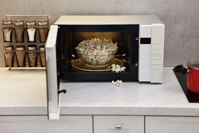 Photo of Open microwave oven with bowl of popcorn on white marble countertop in kitchen