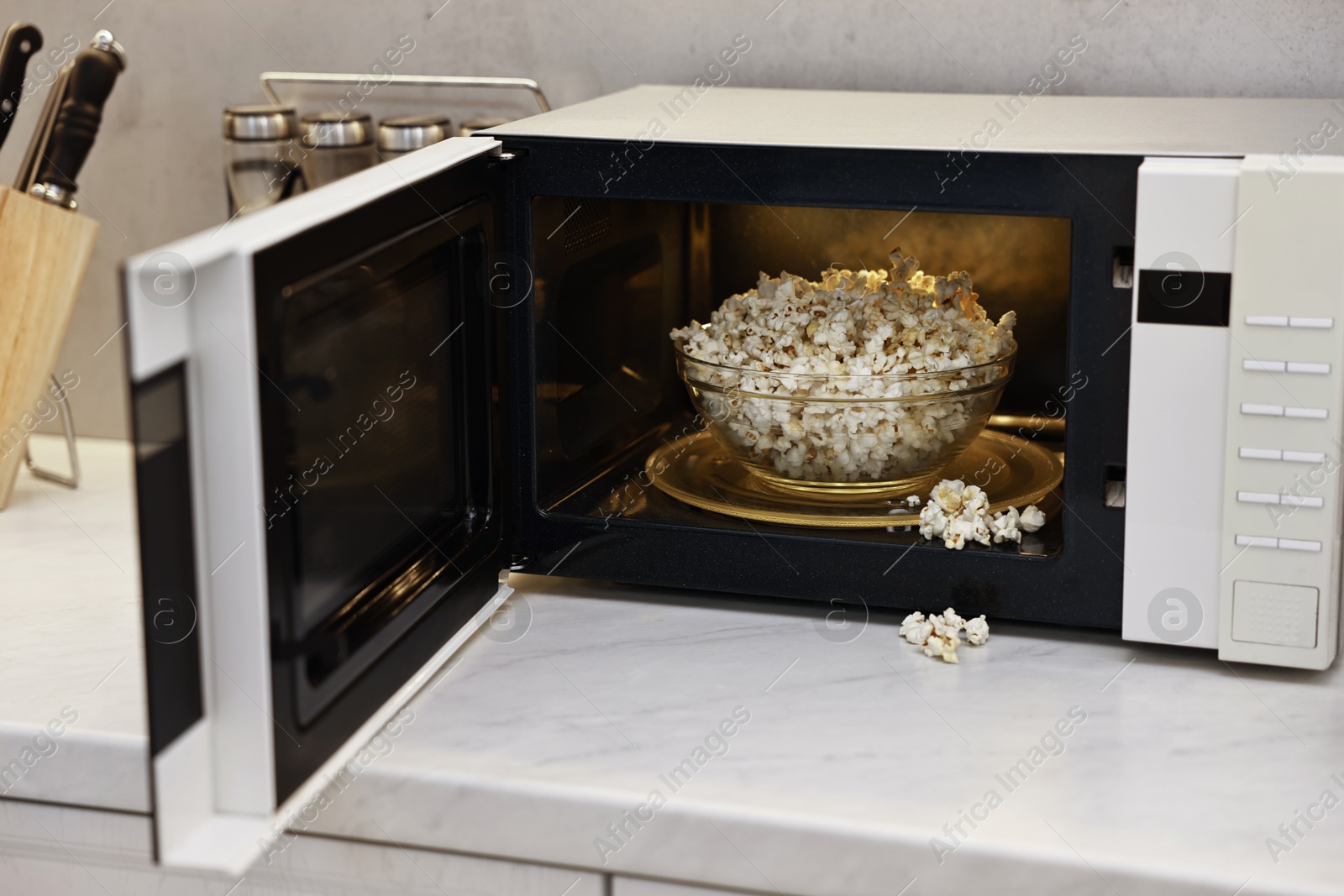 Photo of Open microwave oven with bowl of popcorn on white marble countertop in kitchen