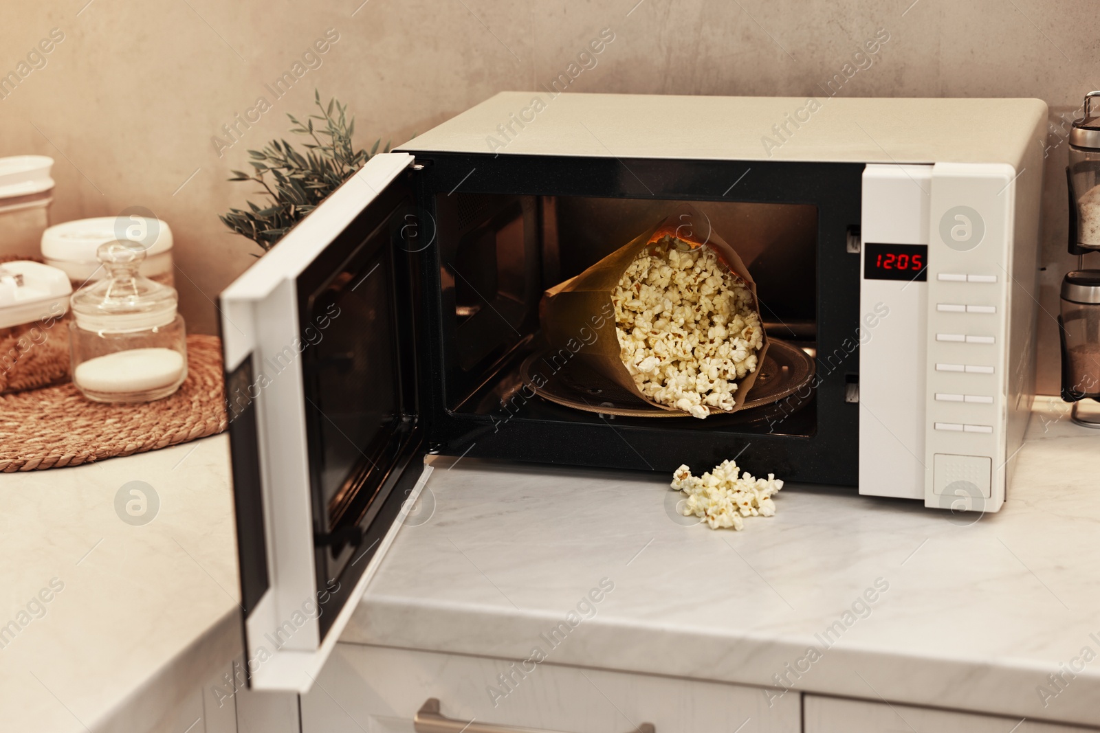 Photo of Open microwave oven with bag of popcorn on white marble countertop in kitchen