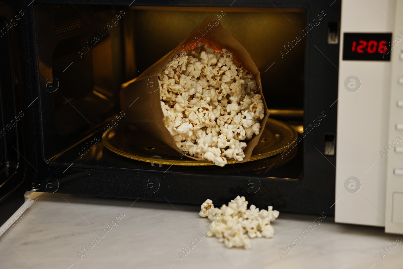 Photo of Open microwave oven with bag of popcorn on white marble table, closeup