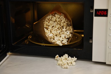 Photo of Open microwave oven with bag of popcorn on white marble table, closeup