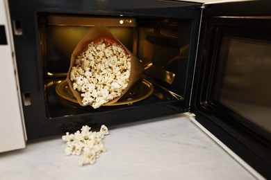 Photo of Open microwave oven with bag of popcorn on white marble table, closeup