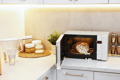 Photo of Open microwave oven with bag of popcorn on white marble countertop in kitchen