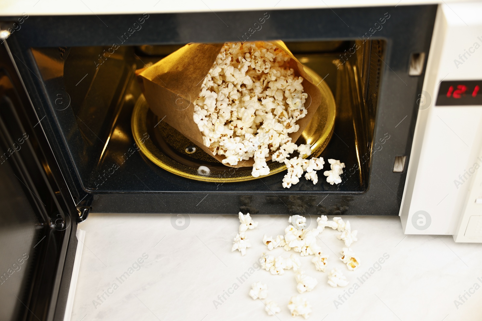 Photo of Open microwave oven with bag of tasty popcorn on white marble table, closeup