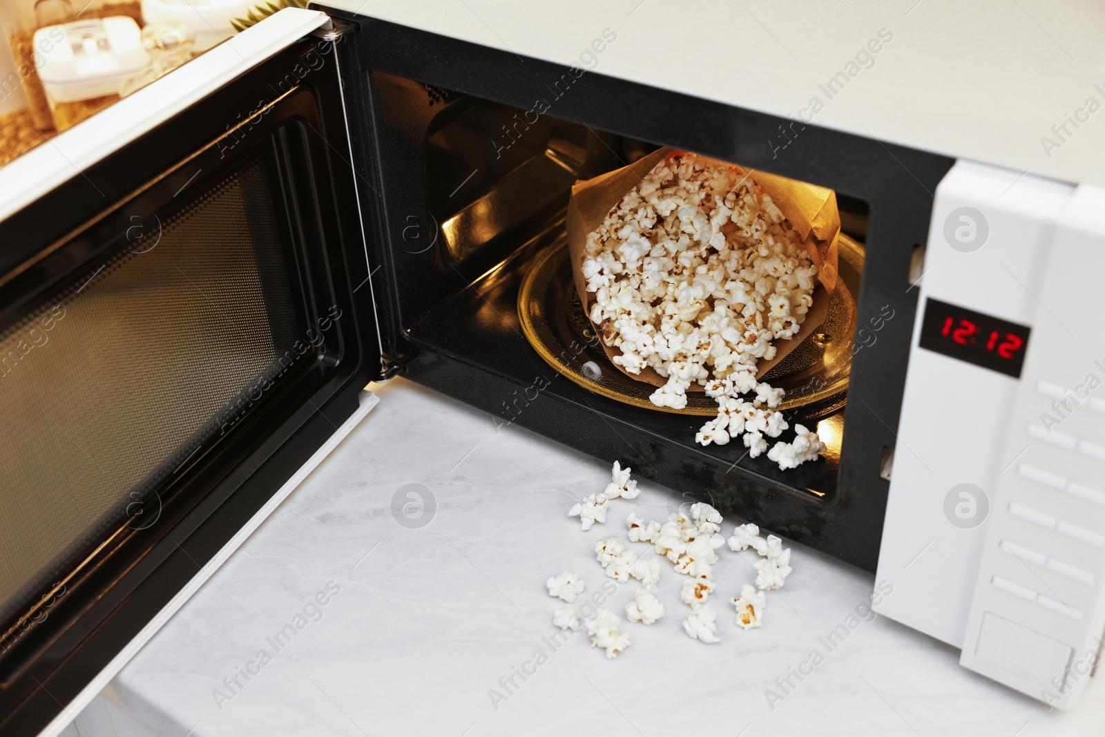 Photo of Open microwave oven with bag of tasty popcorn on white marble table