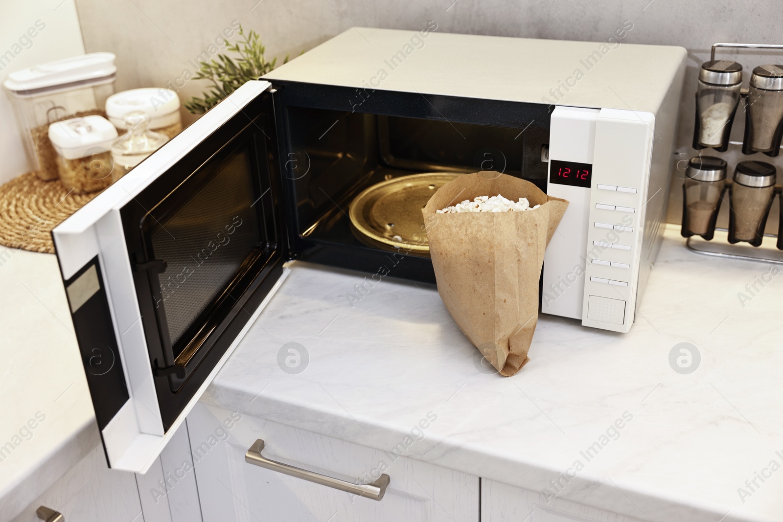 Photo of Tasty popcorn in paper bag near microwave oven on white marble countertop indoors