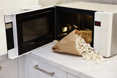 Photo of Tasty popcorn in paper bag near microwave oven on white marble countertop indoors