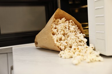 Photo of Tasty popcorn in paper bag near microwave oven on white marble countertop indoors, closeup