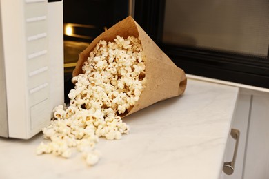 Photo of Tasty popcorn in paper bag near microwave oven on white marble countertop indoors, closeup