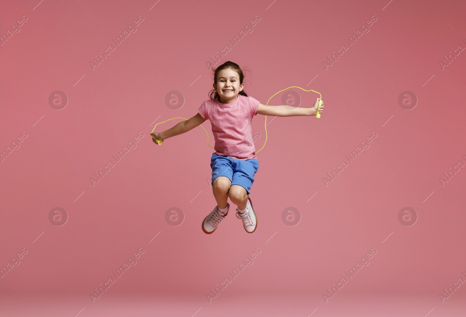 Photo of Cute little girl with jump rope on light pink background