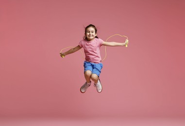 Photo of Cute little girl with jump rope on light pink background