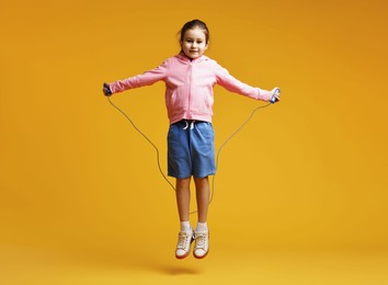 Photo of Cute little girl with jump rope on yellow background