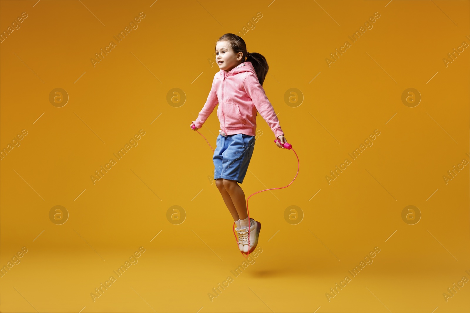 Photo of Cute little girl with jump rope on yellow background