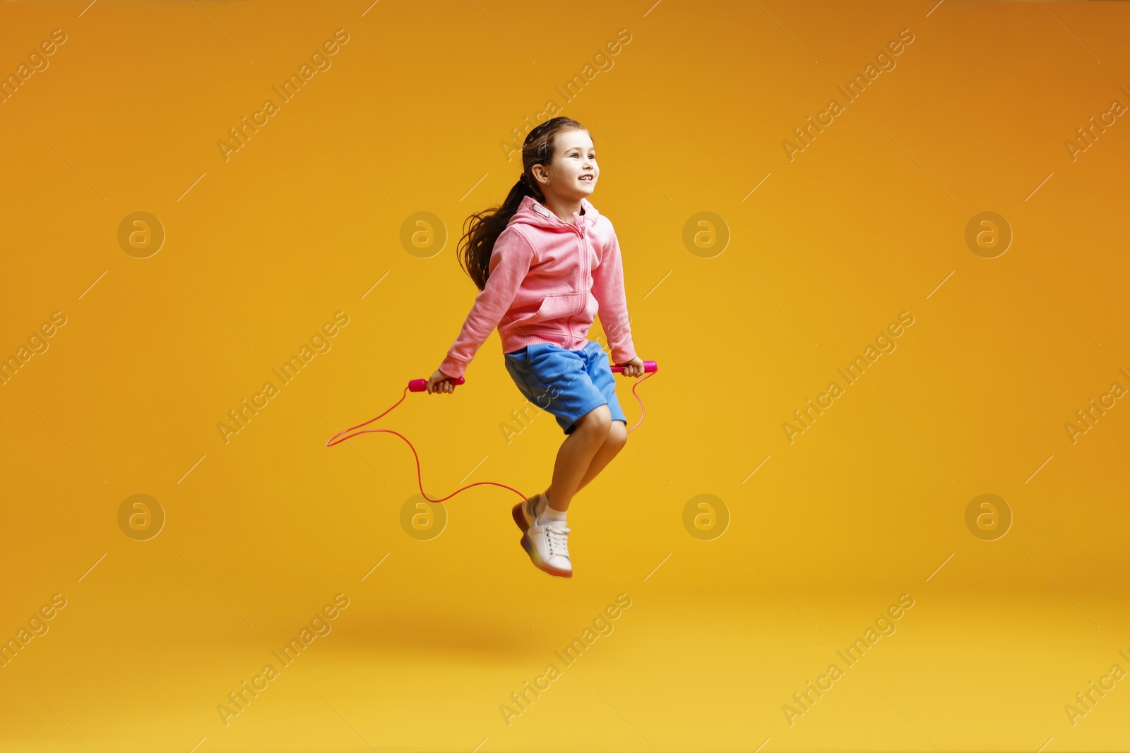 Photo of Cute little girl with jump rope on yellow background