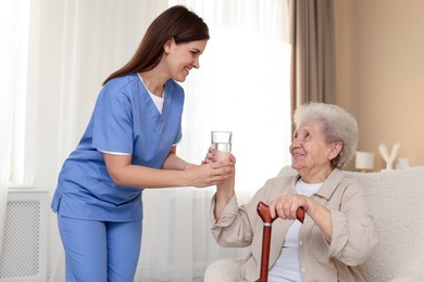 Healthcare worker giving elderly woman glass of water indoors