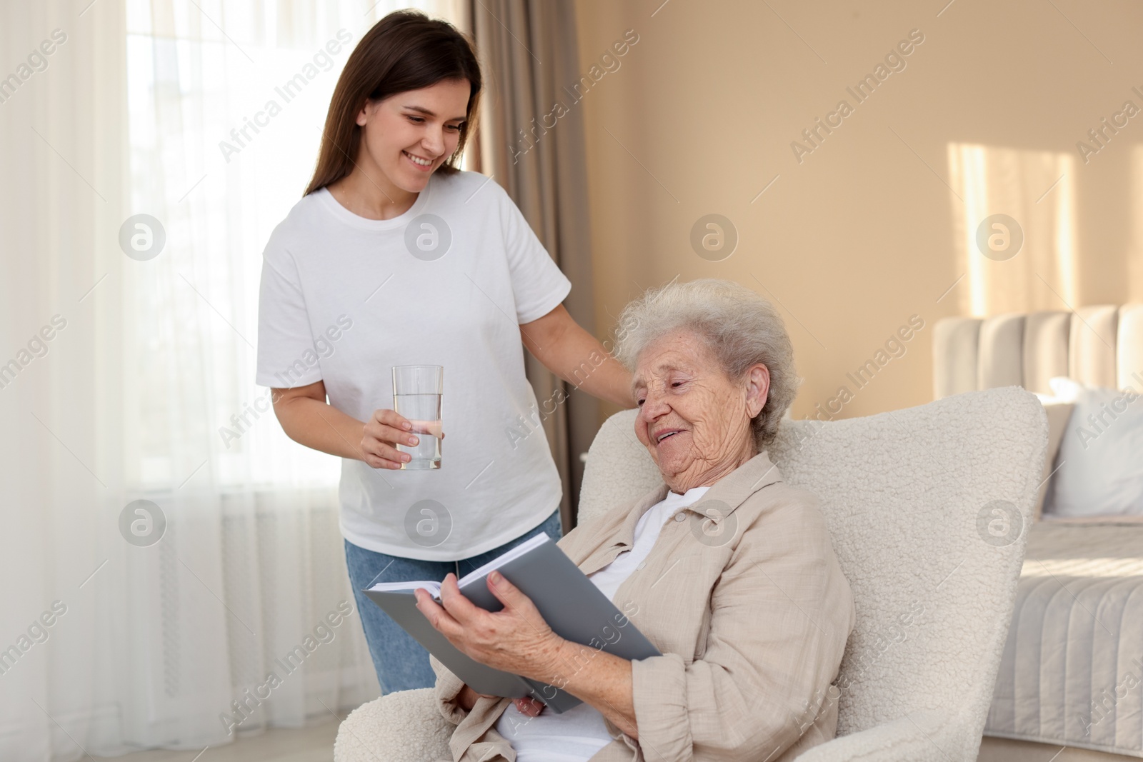 Photo of Granddaughter giving glass of water to her grandmother at home. Elderly care