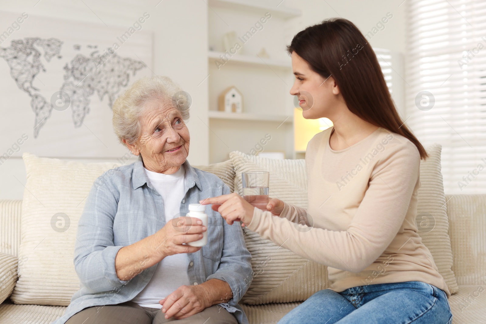 Photo of Granddaughter giving pills and glass of water to her grandmother at home. Elderly care