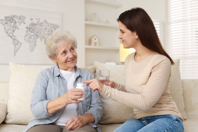 Photo of Granddaughter giving pills and glass of water to her grandmother at home. Elderly care