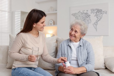 Photo of Granddaughter giving pills and glass of water to her grandmother at home. Elderly care