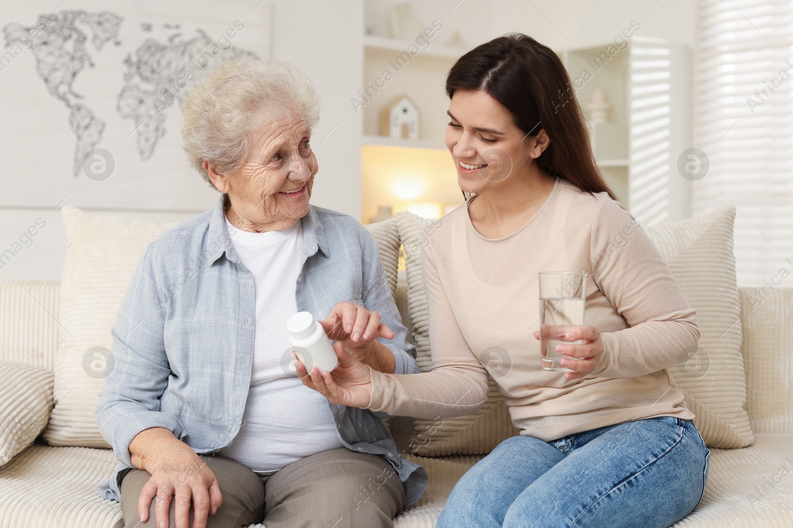 Photo of Granddaughter giving pills and glass of water to her grandmother at home. Elderly care