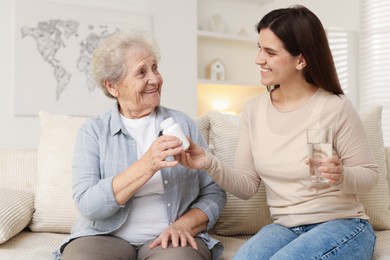 Granddaughter giving pills and glass of water to her grandmother at home. Elderly care