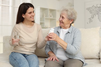 Granddaughter giving pills and glass of water to her grandmother at home. Elderly care