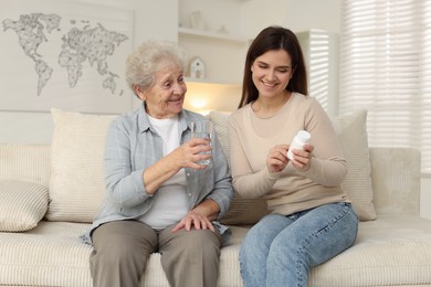 Granddaughter with pills and her grandmother on sofa at home. Elderly care