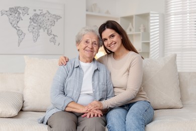 Photo of Happy granddaughter with her grandmother on sofa at home. Elderly care